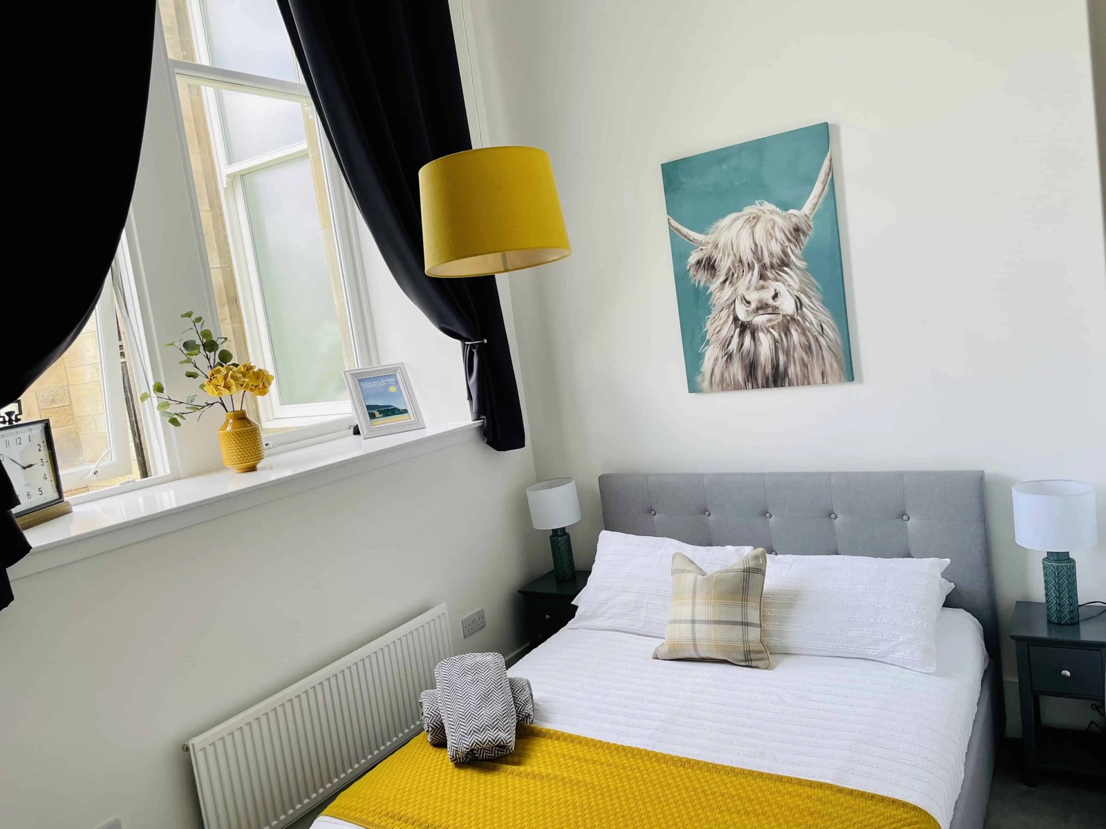 Double bedroom with Highland cow painting, grey upholstered bed and yellow throw